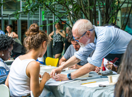 A Metalwerx instructor leans over a table where three students are sitting down working