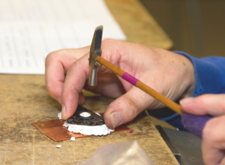 Two hands hold a tiny jewelry hammer to alter a small piece of metal