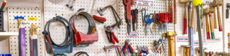 Metalsmithing and jewelry tools hang on a corkboard wall including shears, sawframe, pliers, and hammers