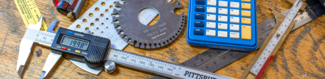 Various measuring tools, gauges, and a calculator are scattered on top of a wooden table surface